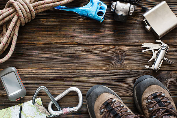 Travel equipment for mountain trip on wood floor. Top view Top view of travel equipment for a mountain trip on a rustic dark wood floor with empty space in the middle. Items include flask, map, knife, rope, carabiner, flashlight, shoes, GPS model kit stock pictures, royalty-free photos & images