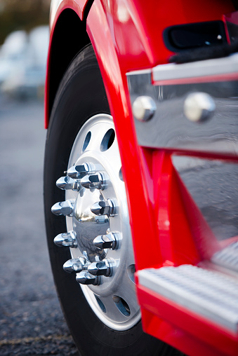 The powerful front wheel on the steering axle of the truck on a powerful modern aluminum wheels with chrome mounting bolts. Detail of a red truck with a wing and chrome complements the steps of the magnitude of this giant.