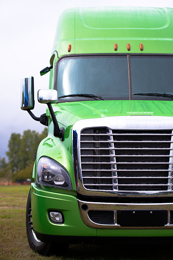 Wet from the rain stylish modern powerful green big rig semi truck with the latest model of commercial long-distance transport in the parking lot waiting for work on highway.
