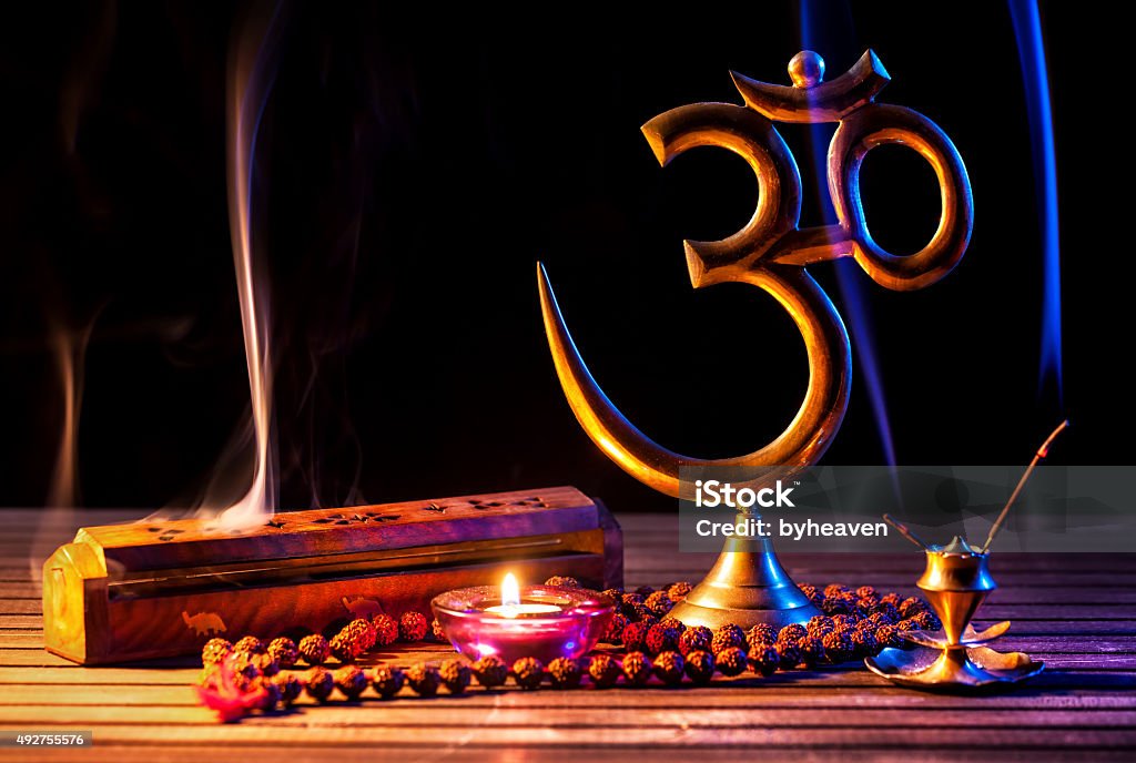 Om shanti Om symbol, incense smoke, candle and japa mala on wooden table at black background Om Symbol Stock Photo