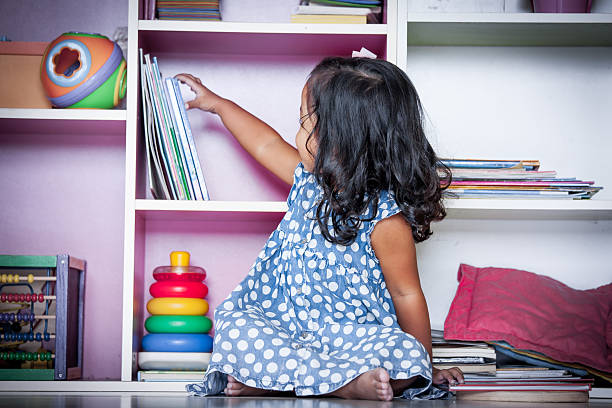 cute little girl selecting a book on bookshelf and stock photo