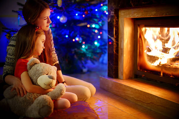 istock Young mother and daughters sitting by a fireplace on Christmas 492764206