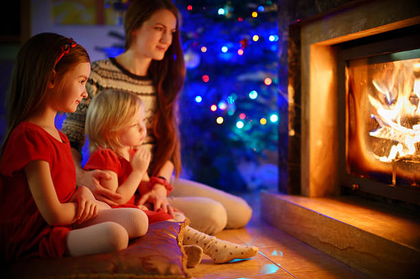 istock Young mother and daughters sitting by a fireplace on Christmas 492764242
