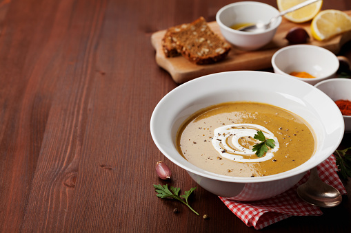 Lentil cream soup in a bowl with spices turmeric, paprika and garlic on wooden table