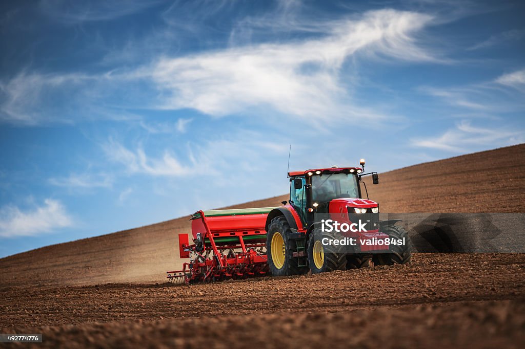 Farmer with tractor seeding crops at field Farmer in tractor preparing farmland with seedbed for the next year Tractor Stock Photo