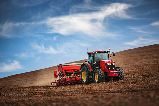 Farmer with tractor seeding crops at field Farmer in tractor preparing farmland with seedbed for the next year agricultural machinery stock pictures, royalty-free photos & images