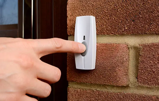 Close-up of woman pressing the button of a doorbell on a brick wall