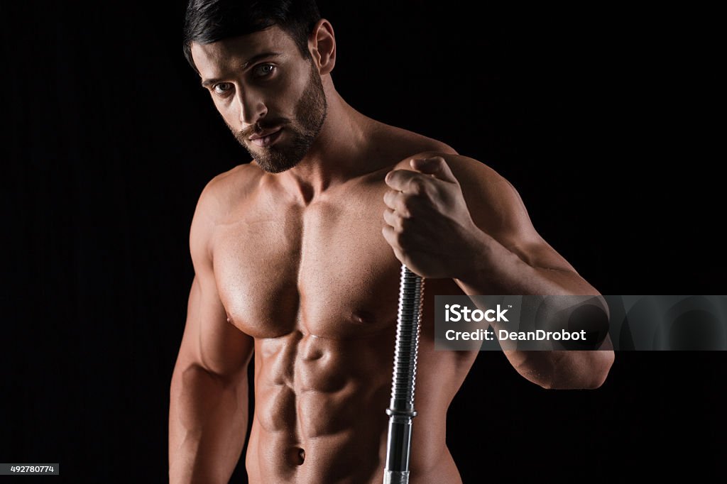 Fitness muscular man holding barbell Portrait of a fitness muscular man holding barbell on black background 2015 Stock Photo