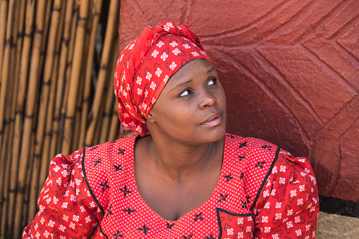 Johannesburg, South Africa - July 04, 2015: woman Bantu nation in handmade red dress and African hat next to her house.