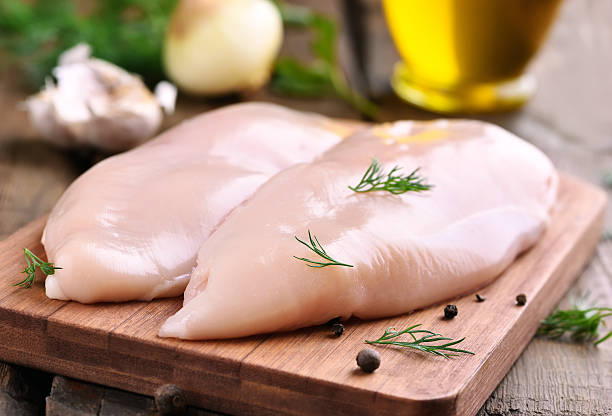 Chicken breasts on cutting board Raw chicken breasts and spices on wooden cutting board, close up view chicken meat stock pictures, royalty-free photos & images