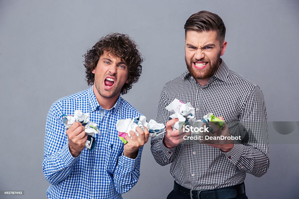 Two angry men with crumpled paper Portrait of a two angry men with crumpled paper over gray background 2015 Stock Photo