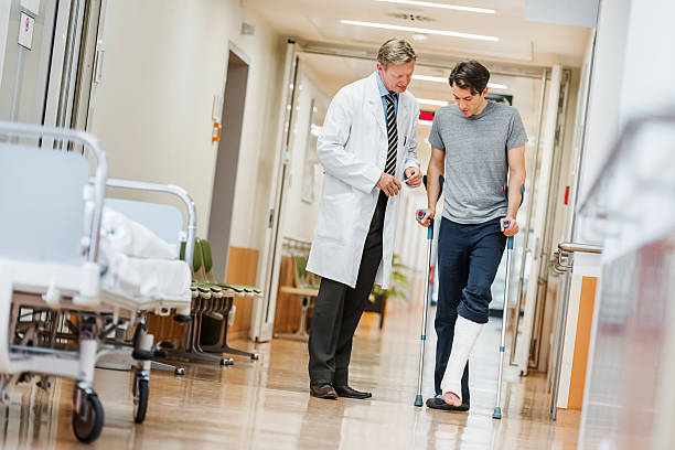 Doctor and Patient in Hospital Man with broken leg talking with doctor in hospital corridor. crutch stock pictures, royalty-free photos & images