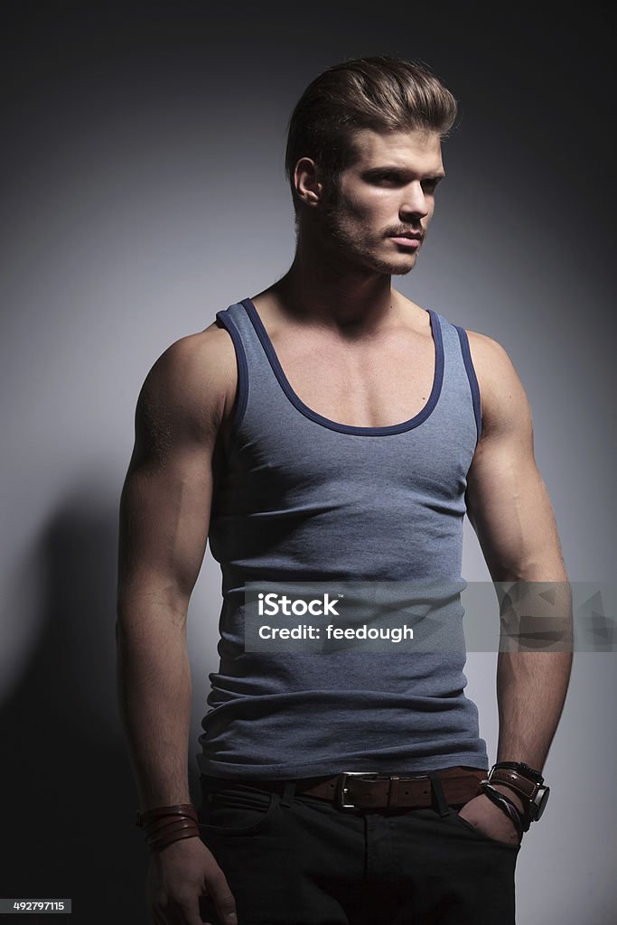 muscular man with hand in pocket muscular young casual man looking away from the camera while holding a hand in his pocket. on a gray background Adult Stock Photo