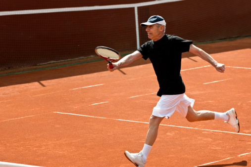Active senior tennis player running for ball