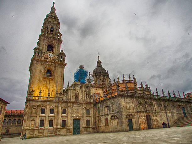 Cathedral clock tower and street view  in Santiago de Compostela, Galicia, Spain. Stone arch frame in the upper part of the image, perspective of row of houses with traditional galerias. Clear sky.