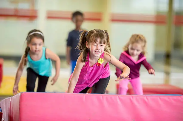 A group of little girls are crawling over a mat and playing in gymnastics class.