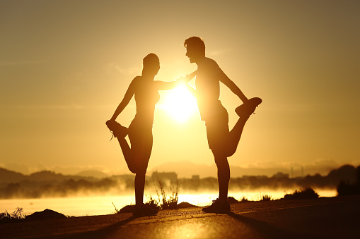 Silhouette of a fitness couple profile stretching at sunset with the sun in the background
