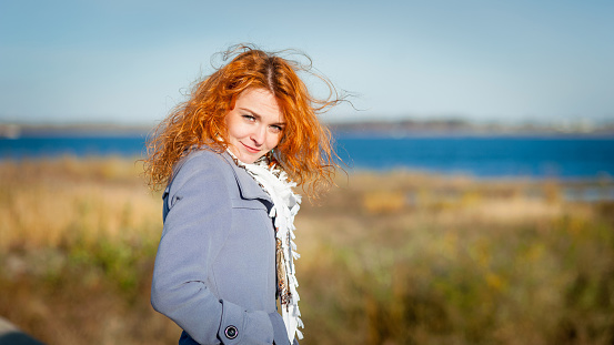 Nice red-haired girl outdoors, river, autumn background.