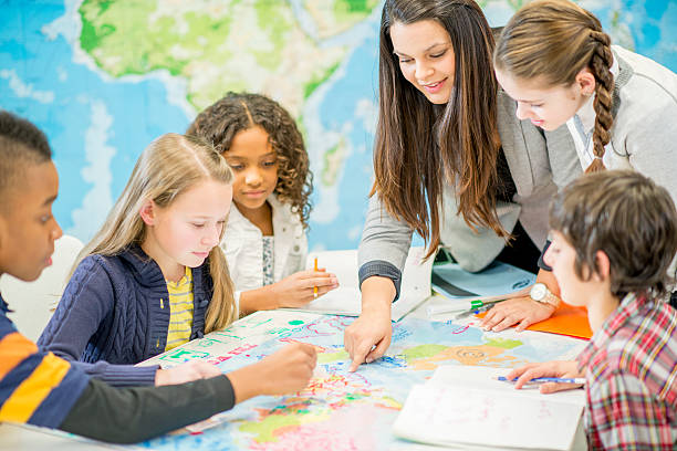 Learning Geography in Class A multi-ethnic group of elementary age children are sitting at a desk and are drawing on a world map for geography class. The teacher is pointing at the map and teaching them about a country. history stock pictures, royalty-free photos & images