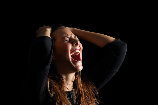 Depressed woman crying and shouting desperately isolated in a black background