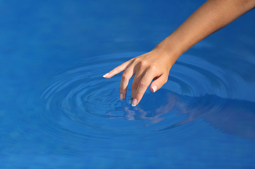 Close up of a woman hand with perfect manicure playing with clean water in a pool with a blue background