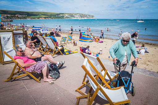 Swanage, UK - August 6, 2015: Senior citizens enjoying the summer sunshine on the crowded beach front of Swanage, the popular seaside holiday resort of Swanage in Dorset, UK. 