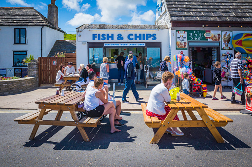 Swanage, UK - August 1, 2015: Holiday makers and tourists enjoying the summer sunshine at table outside a traditional British fish and chip shop on the beach promenade at the popular seaside resort of Swanage, Dorset, UK.