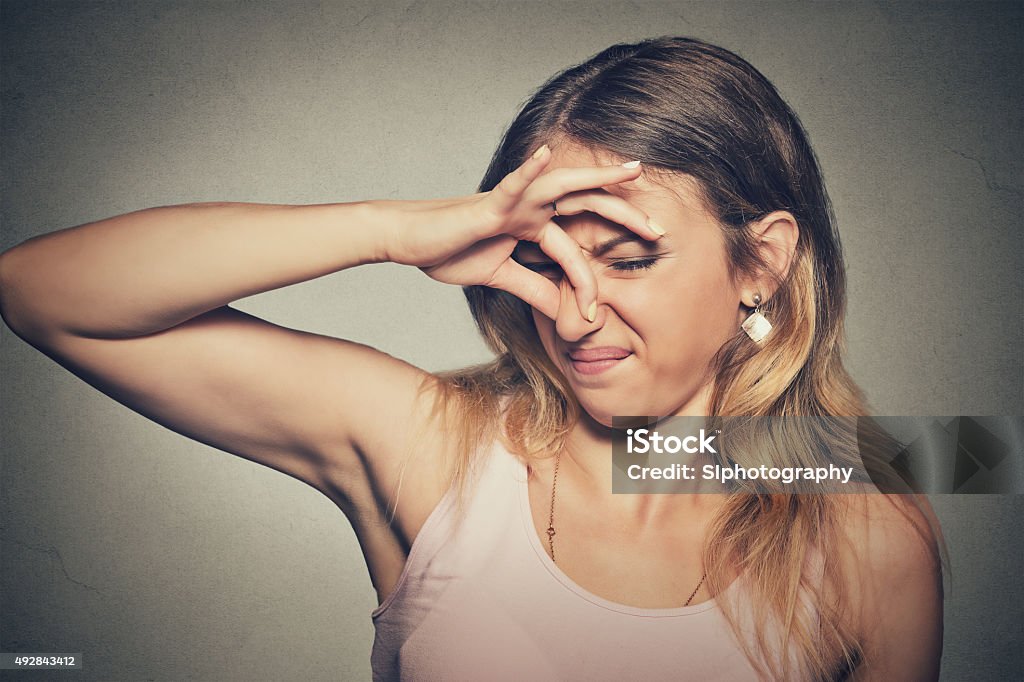 woman pinches nose looks with disgust stinks bad smell Closeup portrait headshot woman pinches nose with fingers hands looks with disgust something stinks bad smell situation isolated on gray wall background. Human face expression body language reaction Unpleasant Smell Stock Photo