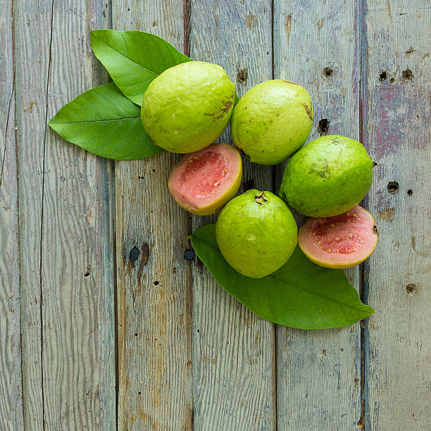 ripe guava fruits and real guava tree leaves over wooden background.