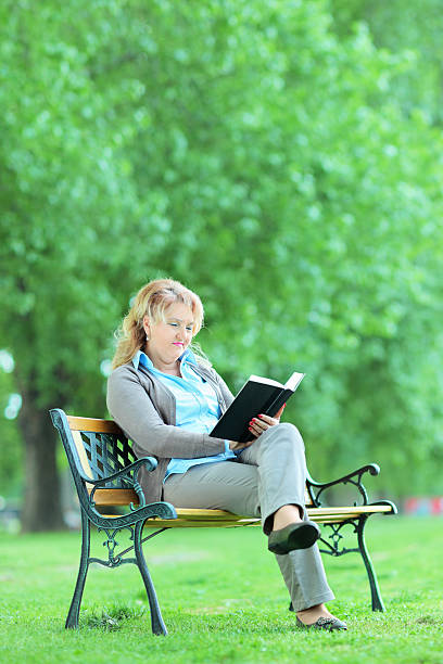 istock Mature lady reading a novel seated on bench 492861537