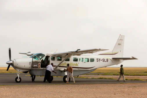 Amboseli, Kanya - March 21, 2014:  Small airplanes land on this strip in the middle of the savannah to pick up tourists for transport between the East African game reserves and Nairobi. Here the African staff is getting the plane ready for departure with the pilot directing.