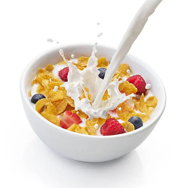 pouring milk into bowl of corn flakes with berry fruits