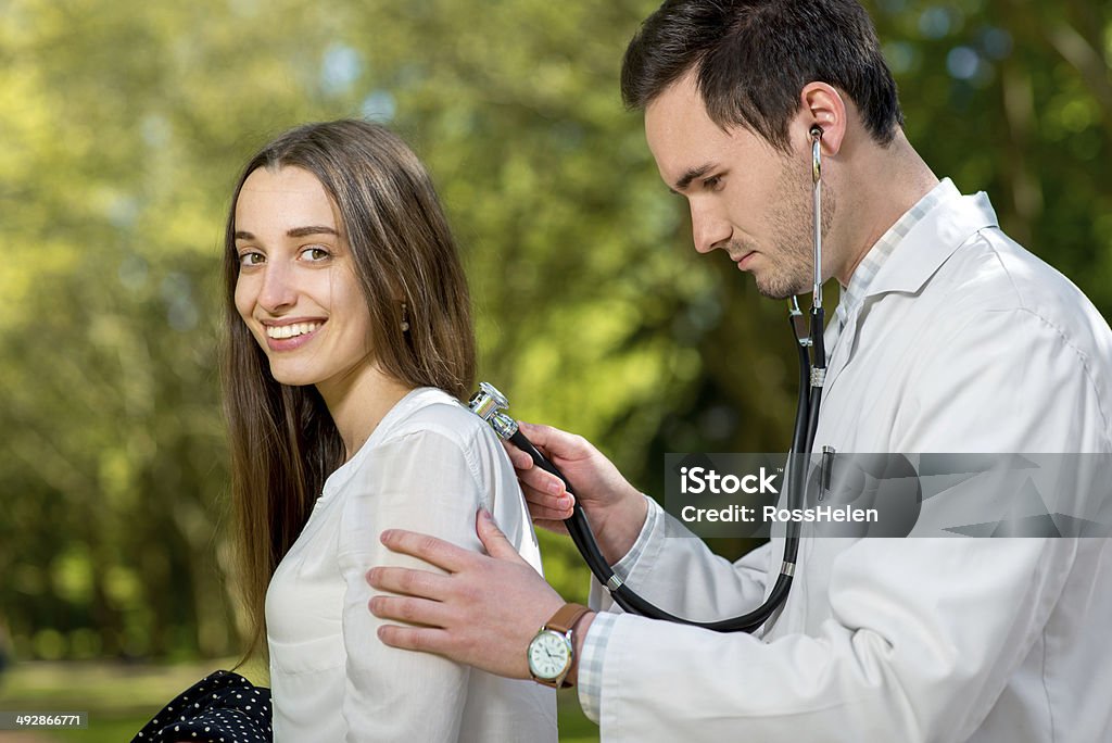 Young doctor listnening with stethoscope  in the park Young doctor listnening with stethoscope to the woman in the park Adult Stock Photo