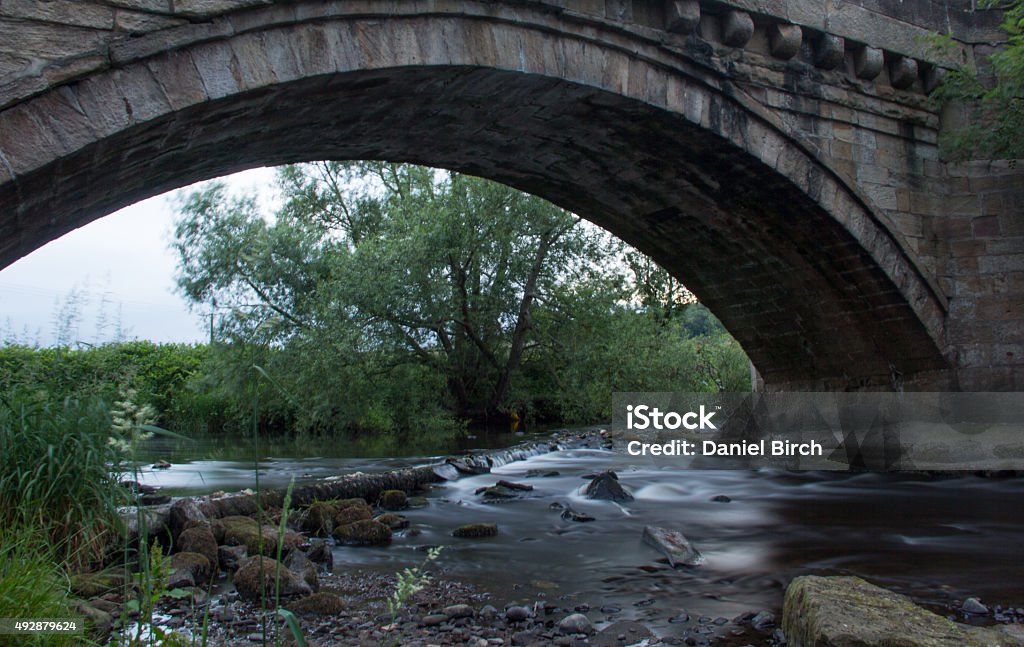 Stream flowing under bridge Long exposure of a stream with a small weir with rocks take in summer at  Hampsthwaite  Yorkshire, England 2015 Stock Photo