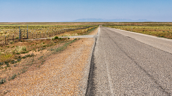 Gravel road intersection turning off into the prairie from a long, flat, straight summer desert highway in Utah, USA.