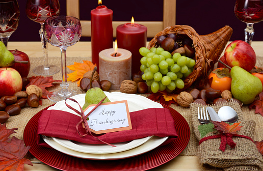 Country style rustic Thanksgiving table with place setting, cornucopia, candles and Autumn fruit centerpice.