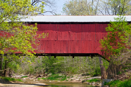 The red Wilkins Mill Covered Bridge spans Sugar Creek in rural Parke County, Indiana near Rockville.