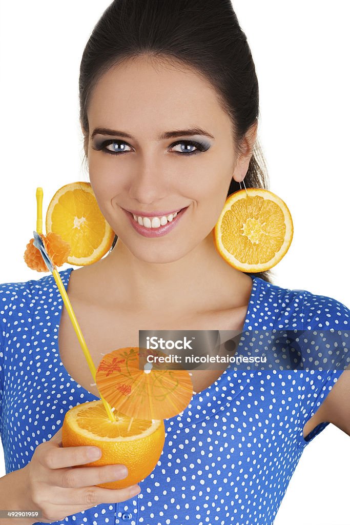Girl with Orange Drink and Orange Slice Earrings White Background Young woman with orange slice earrings holding a sliced orange with a straw on white background Adult Stock Photo