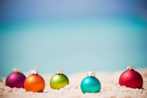 Christmas concept: Christmas baubles lying on a tropical beach. Focus on green bauble.