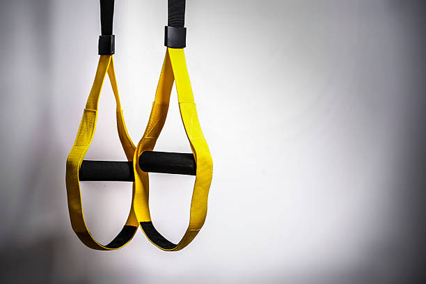 TRX straps Hanging TRX susspension fitness straps used for sports training, shot in a gym next to a white wall with lot of copy space. suspension training stock pictures, royalty-free photos & images