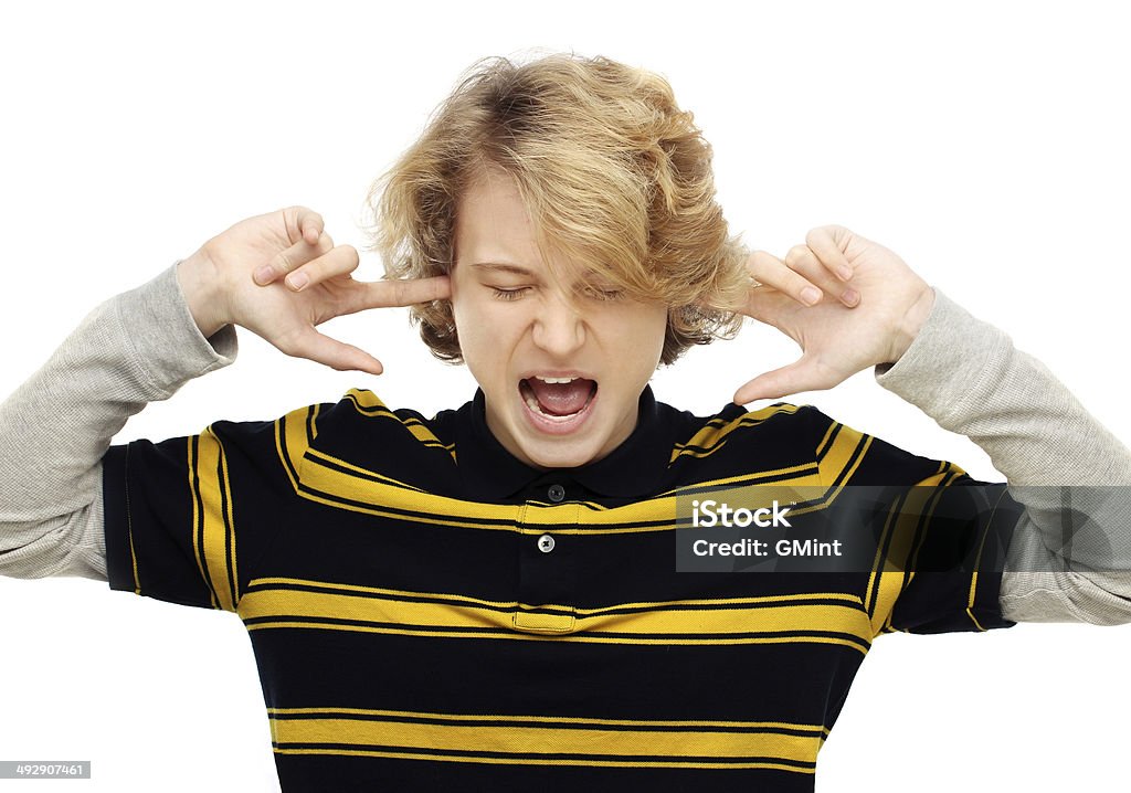 Portrait of furious teenage boy screaming Portrait of furious teenage boy screaming at the camera with his hands covering ears and closing eyes.White background Adolescence Stock Photo