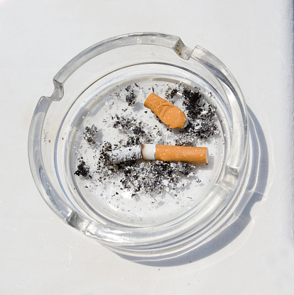 Two butts in glass transparent ashtray on white background