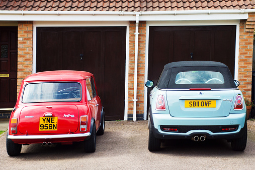 Huntingdon, United Kingdom - August 7, 2015: A rare classic Italian built Innocenti Mini Cooper 1300 export next to a BMW Mini Cooper S convertible on the drive of a residential house. Both have central twin tail pipe exhausts.