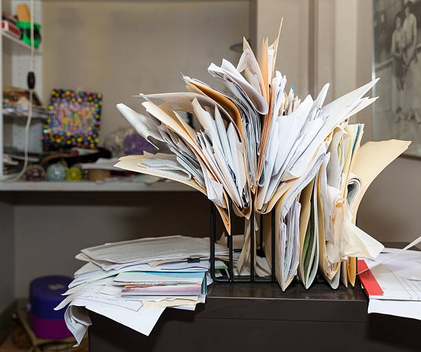 Messy, chaotic, file rack on a desk in cluttered room Example of desk clutter with haphazardly arranged, overstuffed file folders in a rack on a messy desk in a cluttered room. Canon EOS 5DIII, 35mm chaotic stock pictures, royalty-free photos & images