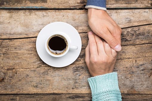 Man holds woman's hand with cup of coffee top view image on wooden backdrop. Friendship coffee background
