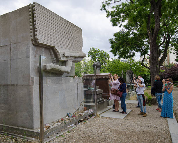 Tomb of Oscar Wilde in Pere Lachaise Cemetery Paris, France - August 16, 2015: Female fans take photos at the tomb of Oscar Wilde, famous Irish playwright who is mourned by “outcast men.” This historic cemetery is one of the most popular tourist attractions crammed with 70,000 grave sites. oscar wilde stock pictures, royalty-free photos & images