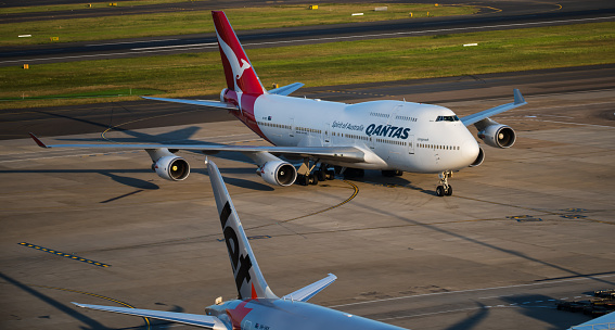  Sydney, Australia October 15, 2015 -Boeing 747-400 in Qantas colour scheme, arriving at Sydney Kingsford Smith airport on a late afternoon. Also visible Commercial Airplane parked, waiting for passengers.
