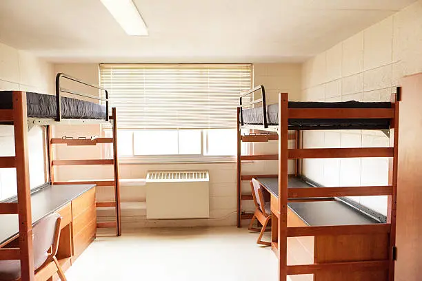 An empty university dormitory room with desk bed and closet.
