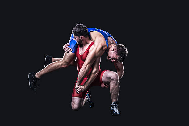 Wrestler performs a throw isolated Two freestyle wrestlers in red and blue wrestling uniform isolated on black background wrestling stock pictures, royalty-free photos & images