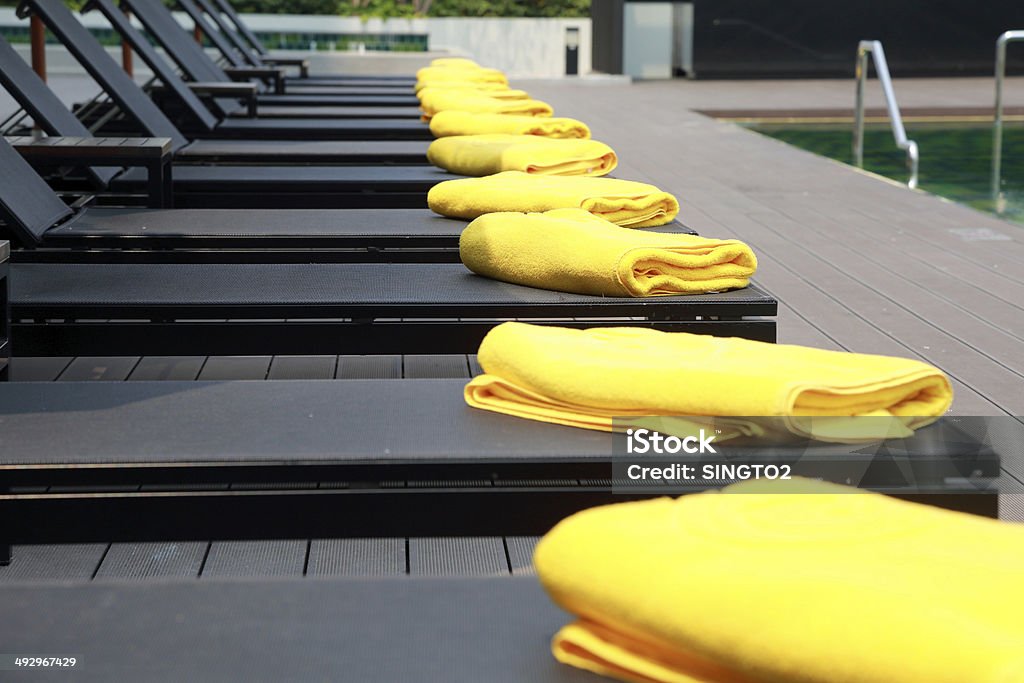 Amarillo, toalla negra sobre las sillas reclinables junto a la piscina del complejo turístico - Foto de stock de Agua libre de derechos